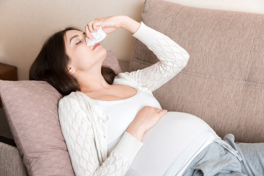 Sick pregnant woman blowing nose into tissue at home Healthy millennial healthcare concept