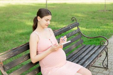 pregnant woman sits on a park bench and writes a to do list to the hospital