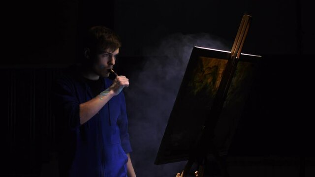 Artist copyist paint seascape with ship in ocean. Vaper smoke vape e-cigarette. Craftsman decorator draw as boat sail on blue sea with acrylic oil color. Draw finger, brush, knife palette. Indoor.