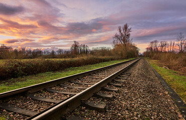 Train track in countryside at sunset with colorful sky and clouds in Rastatt, Germany.
