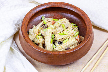 Asian fuzhu salad (yuba sticks, soy bean curd, tofu skin) in round wooden bowl on light background.