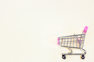 Pink empty shopping cart from the supermarket as a symbol of consumption and consumerism on light background with copy space. Marketing and merchandise concept.