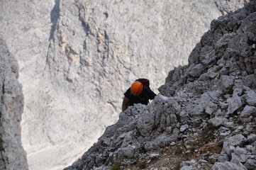 Człowiek w pomarańczowym kasku na ferracie w Dolomitach, Włochy - obrazy, fototapety, plakaty
