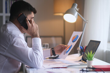 Busy male businessman talking on Cellphone and checking financial reports at home, Young businessman making phone call and working with documents.