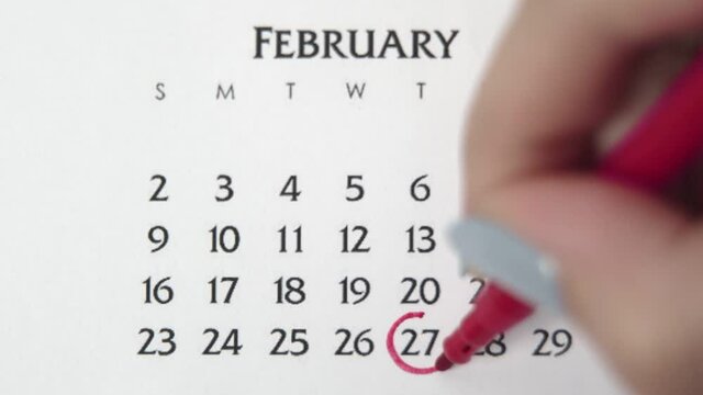 Female hand circle day in calendar date with a red marker. Business Basics Wall Calendar Planner and Organizer. FEBRUARY 27th