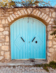 Old blue painted wooden door and stone wall with lanterns on both sides. Old Mediterranean style of Datca, Turkey.