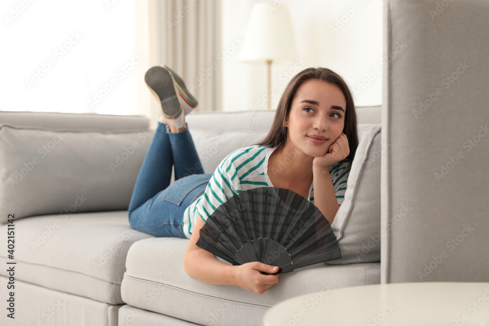 Wall mural Woman enjoying air flow from hand fan at home. Summer heat