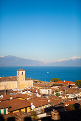 Aerial view of the snow-capped Italian alps, Garda lake and small european buildings with orange tiled roofs, towers and chimneys. Panorama of Desenzano del Garda, Lombardy, Italy.