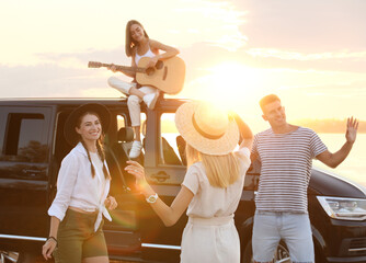 Happy friends having fun near car outdoors at sunset. Summer trip