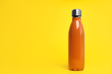 Stylish thermo bottle on yellow background, space for text