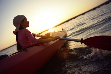Little girl kayaking on river at sunset. Summer camp activity