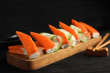 Wooden board with cut crab sticks and cucumber on table
