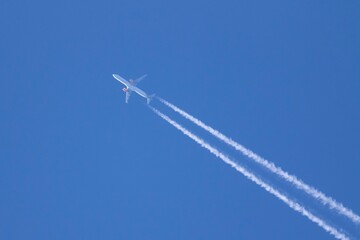 A portrait of an airplane flying through the sky with the condensation trails, contrails or vapour trails behind it. The plane is crosing from one corner to the other in a blue sky.