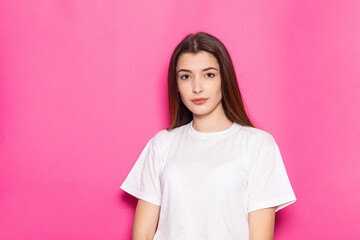 Smiling young brunette woman girl in casual white clothes, posing isolated on pastel pink background studio portrait. People emotions lifestyle concept. Mock up copy space. Looking camera