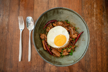 Marinated chili pork with fried egg in ceramic bowl and cutlery on the table