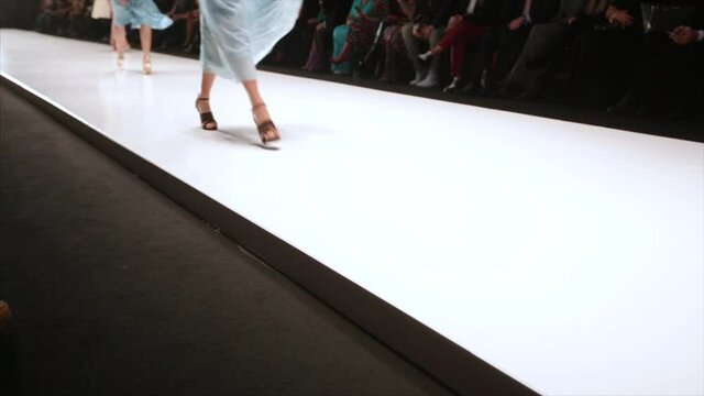 Out of focus background, models walk the runway during fashion show.