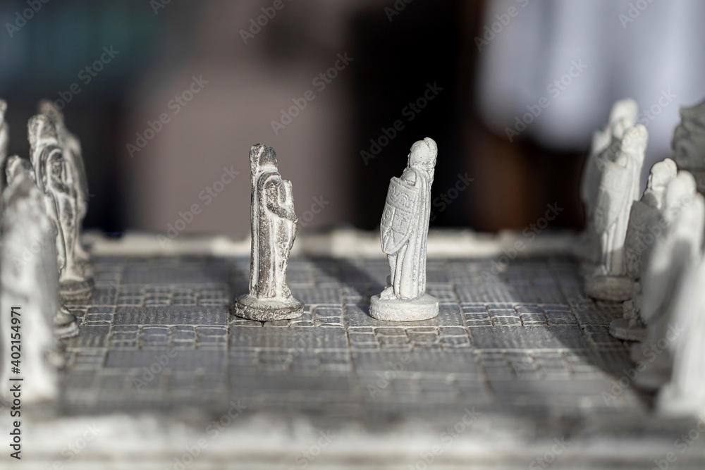 Wall mural A side view portrait of two pawns facing eachother in the beginning of a strategic game of chess. The duel will be fought on a stone chessboard with stone sculptures as the chess pieces.