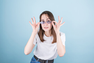 Portrait of a surprised young beautiful girl with glasses looking at the camera with her glasses down. Isolated on blue background