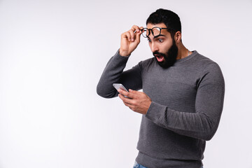 Excited shocked young Arabian man with smart phone isolated over white background
