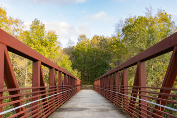 A red iron pedestrian bridge leads over a river into the woods on the Neuse River Greenway in...
