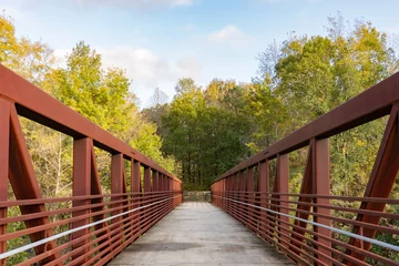 Gardinen Brücken A red iron pedestrian bridge leads over a river into the woods on the Neuse River Greenway in Raleigh, North Carolina, USA  © Liz W Grogan