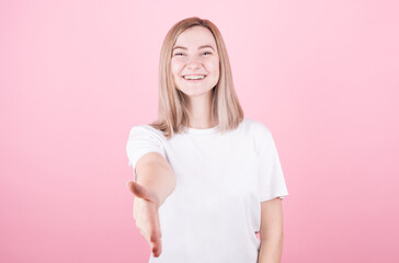 Young woman over isolated pink background shaking hand to make a good deal