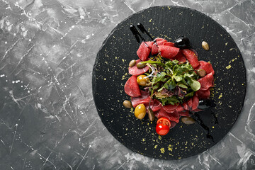 Beef carpaccio with arugula on a black plate, traditional Italian cuisine. Dark key, copy space,