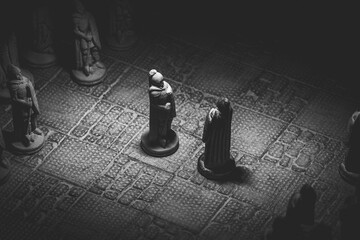 A black and white portrait of two soldier pieces of a game of chess facing each other in the...