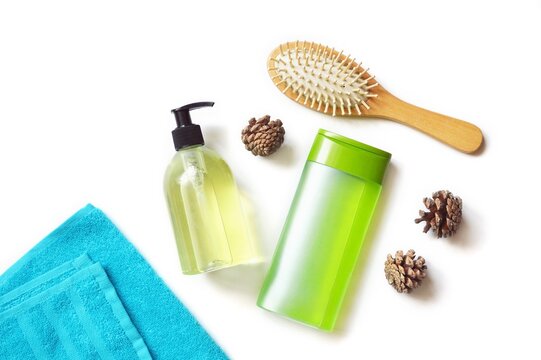 Liquid soap package, green shampoo bottle, wooden hairbrush, blue towel and pine cones isolated on a white background. Hair care cosmetic products flat lay photo