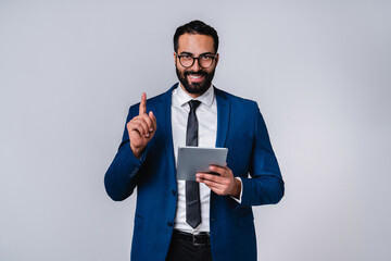 Smart formal Arab businessman in office attire with tablet pointing at copy space isolated over grey background