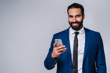 Portrait of a young smiling middle eastern man in business suit using mobile phone isolated over...
