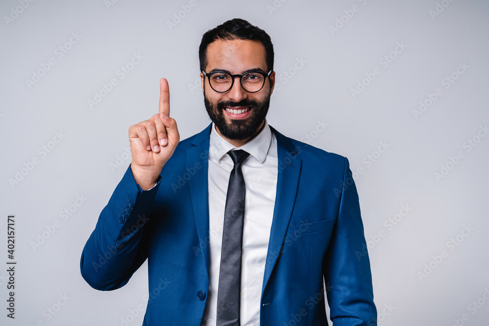 Poster Smiling 25s middle eastern businessman in formal attire pointing at copy space isolated over grey background