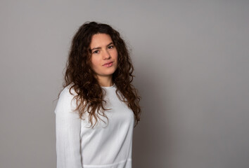 Beautiful young woman with curly and long hair posing in white dress on grey background 