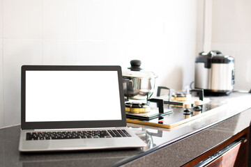 Close up, A notebook computer white screen on the kitchen counter. Has a pot on the gas stove. Blurred background, moke up, clipping path