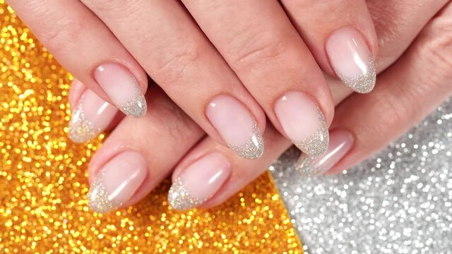 Closeup top view flatlay 4k video of female fingers with beautiful elegant pastel french nail design of pink and silver colors isolated on sparkling golden background with copyspace. Holiday nails.