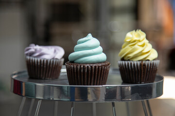 three chocolate cakes decorated with yellow, blue and violet cream on a silver platter, selective focus