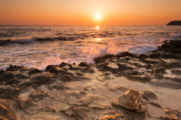 Crushing waves on jagged rocks during sunrise