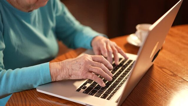 Closeup of elderly womans arthritis hands while she types on laptop computer keyboard.
