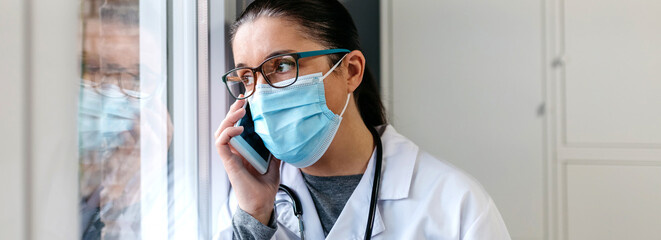 Serious female doctor talking on the cell phone while looking out the window