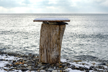 Homemade table on a stump covered with snow on the background of the sea