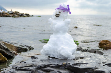 A real snowman with a purple handkerchief on a stone by the sea