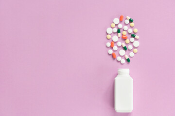 White medical bottle with variegated pills. The concept of insurance medicine, high cost of drugs. Isolated on a pink background.