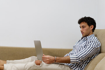 Portrait of a young man working with a laptop while lying on the couch