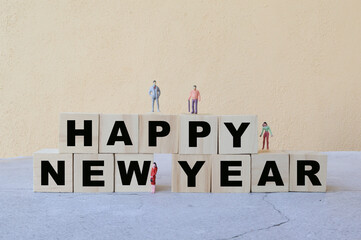 Happy miniature people standing on wooden block written with text Happy New Year.