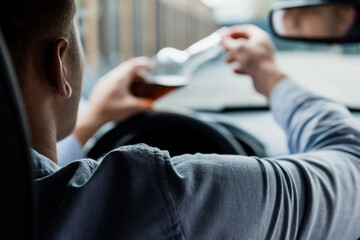 partial view of man opening bottle of alcohol in car, blurred foreground.
