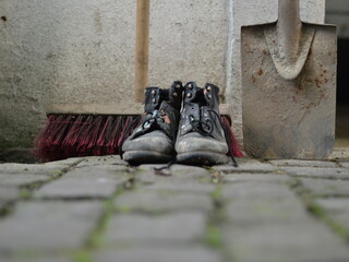 old worn painted work boots with a yard broom and a spade as symbol for cleaning, house keeper or...