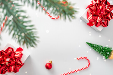 Christmas decoration red background. White gifts with scarlet bow, red balls and sparkling lights in xmas decoration on white background for greeting card. Flat lay, top view, copy space.
