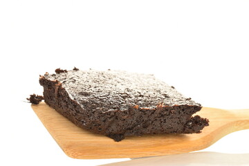 One chocolate brownie with cherries on a wooden spatula, close-up, on a white background.