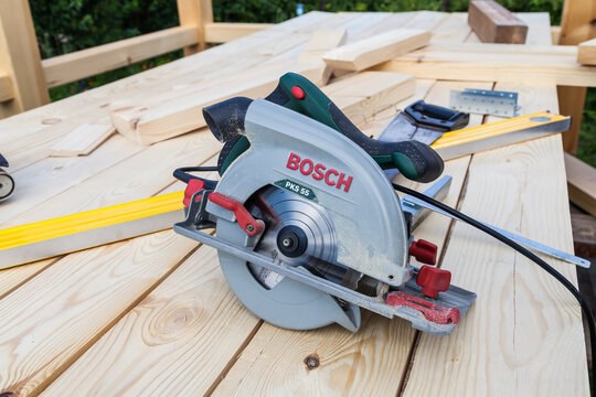 Close-up of a modern new electric hand saw Bosch PKS 55 with a green  plastic case and a metal blade on a wooden beam during the construction  work of a carpenter. Stock