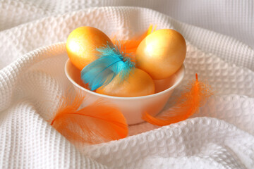  golden eggs on a white cup and golden feathers. Easter celebration concept. There is room for text.